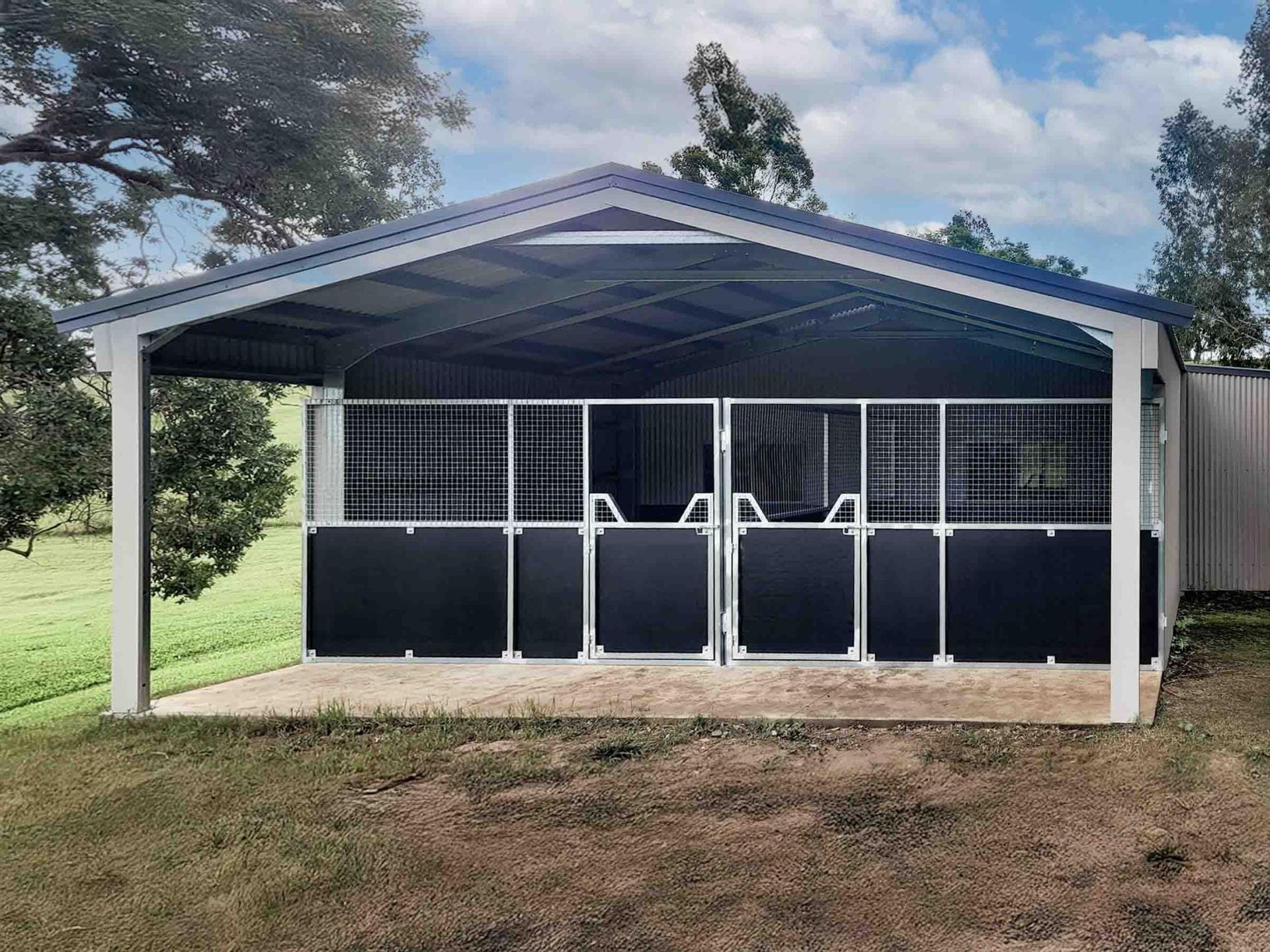 A Large Gray Building With A Black Fence Around It — Equine Stable Solutions In Diddillibah, QLD