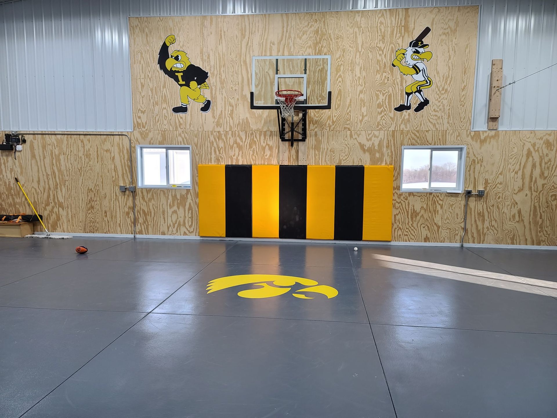Indoor basketball court with black and yellow wall padding and black-and-yellow floor logo.
