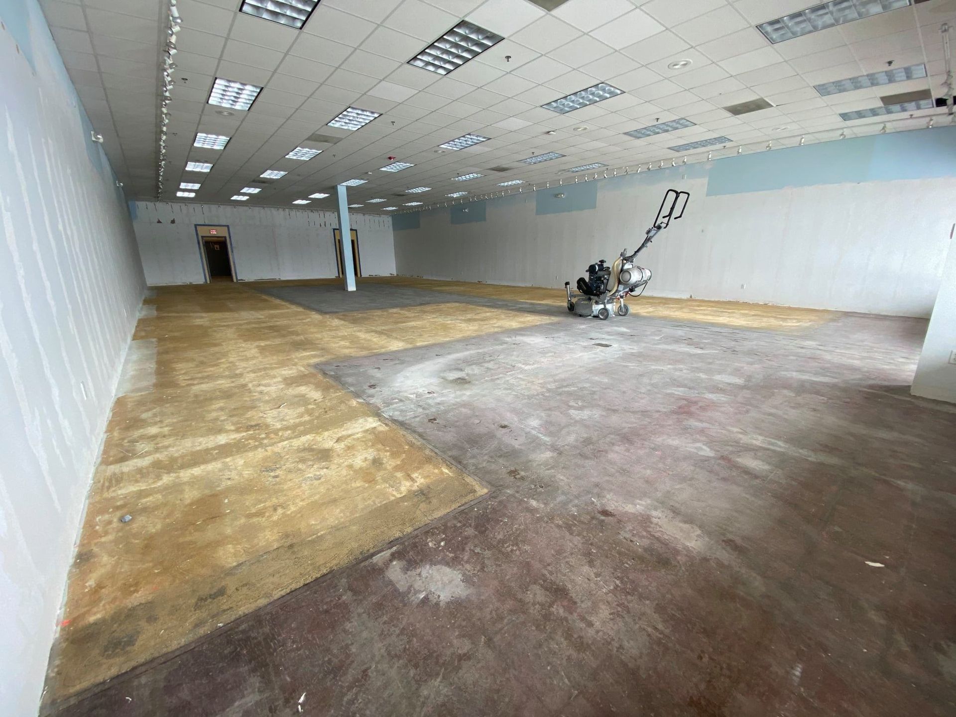 Empty vacant room with white walls, tiled ceiling, and a floor grinder near the back wall