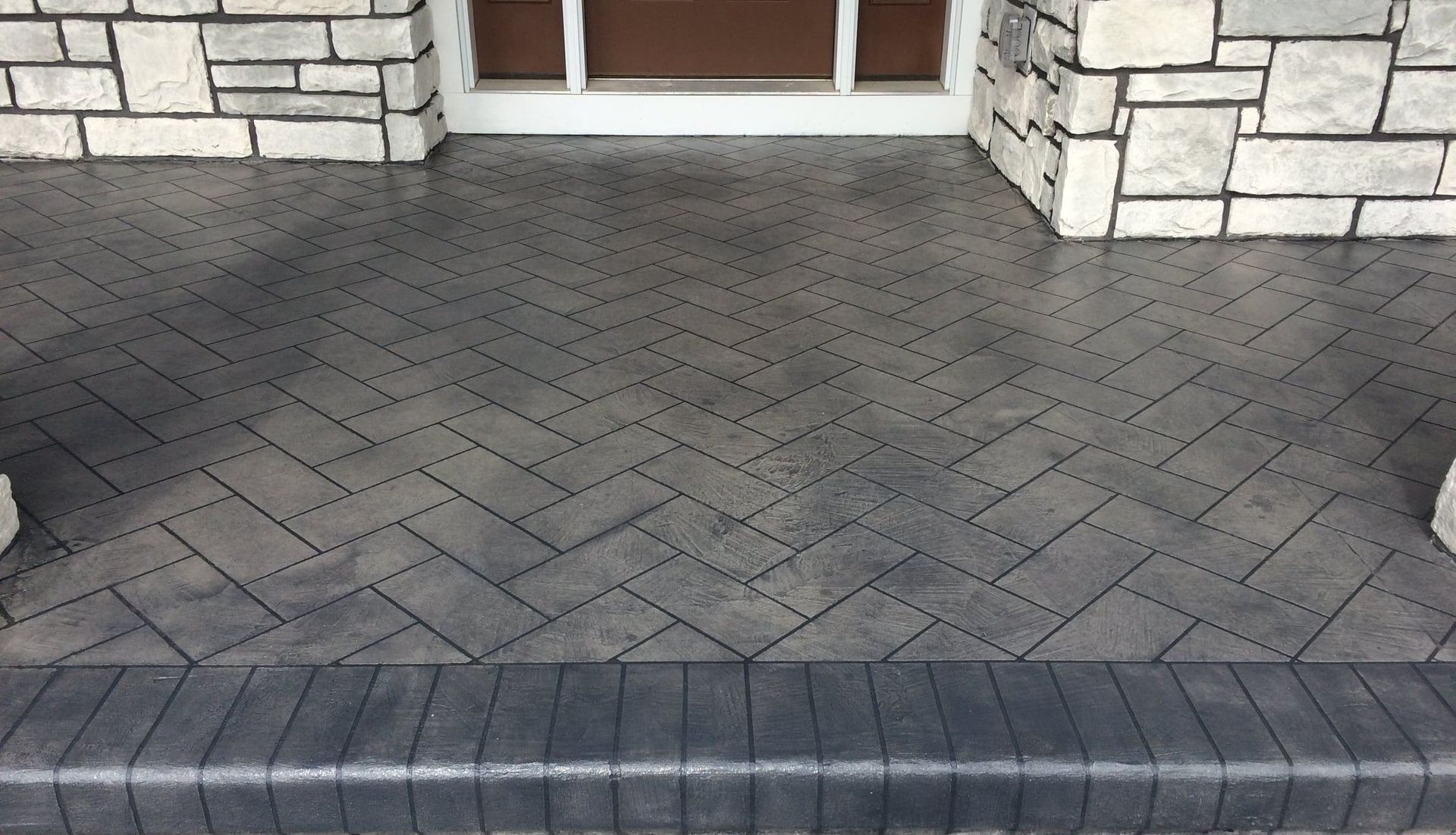 Stone walkway with dark gray herringbone pavers leading to a building entrance.