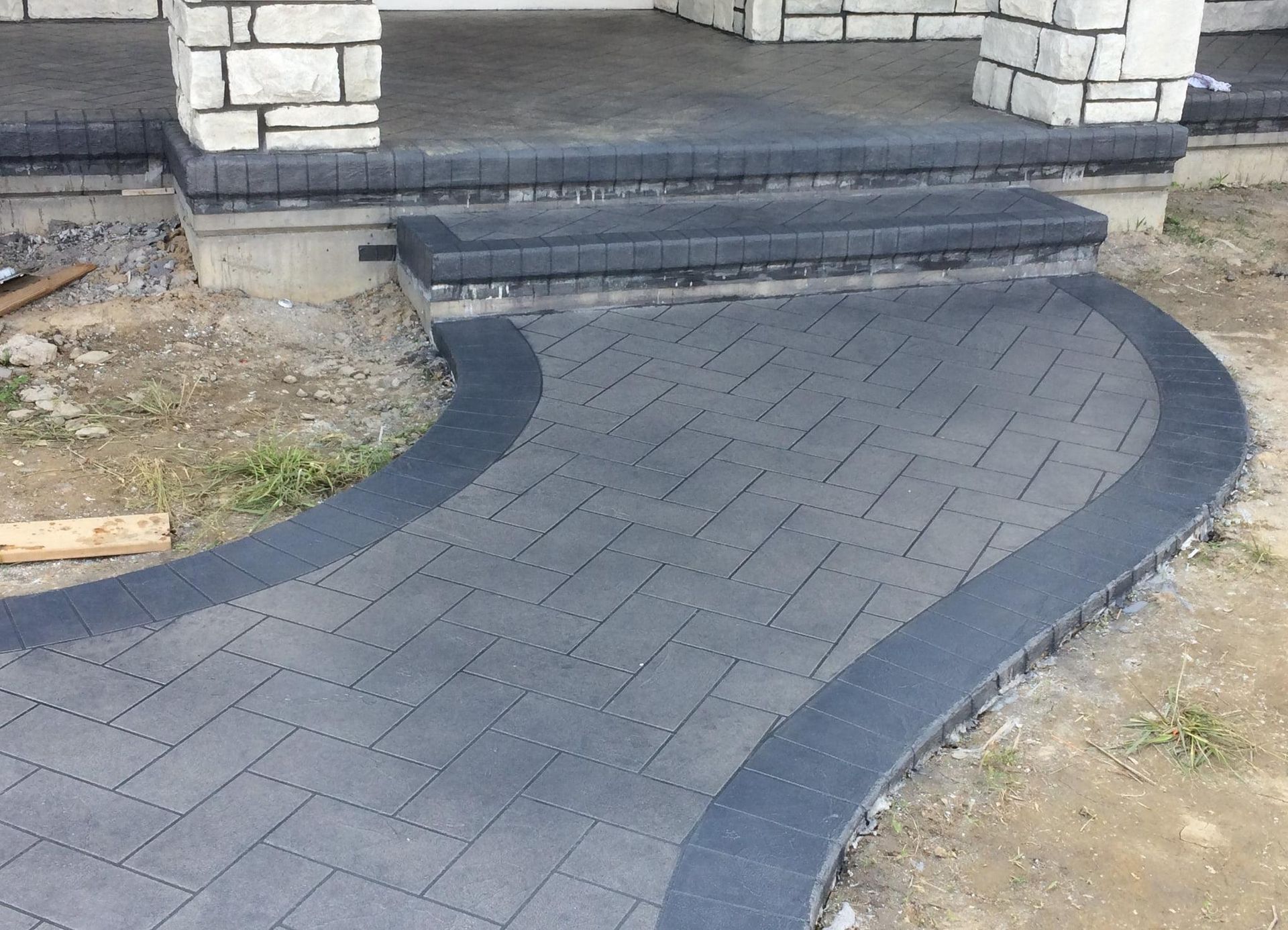 Curved gray brick walkway leading up to a house porch with steps and stone pillars