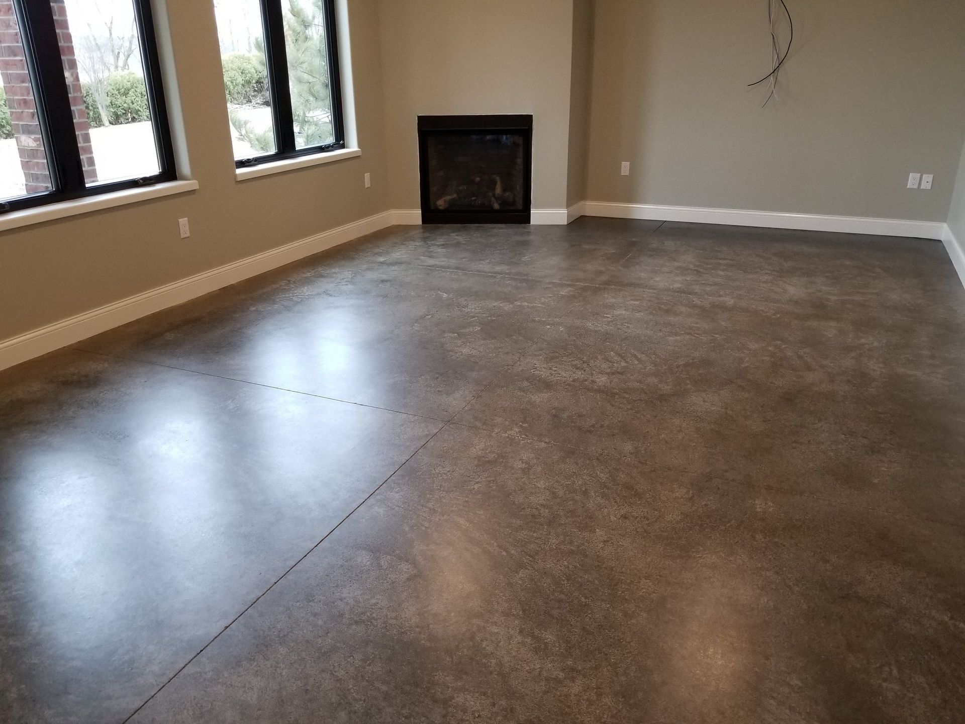 Empty room with polished concrete floor, beige walls, windows, and a small fireplace.