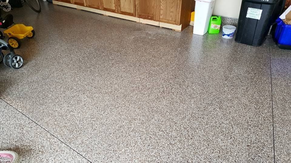 Speckled garage floor with a child’s toy car, cleaning supplies, and storage bins along the wall
