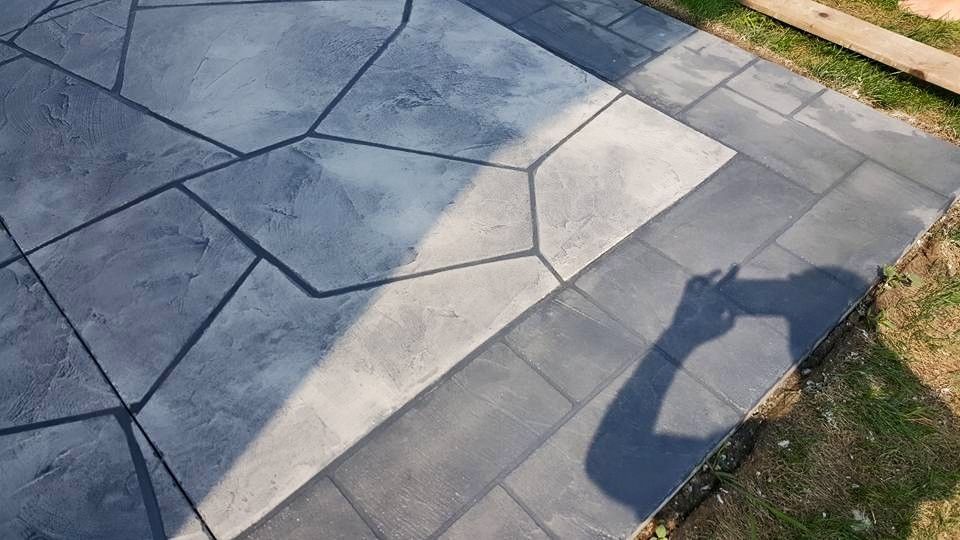 Shadow of a person on a stone patio with geometric gray pavers and grass edge