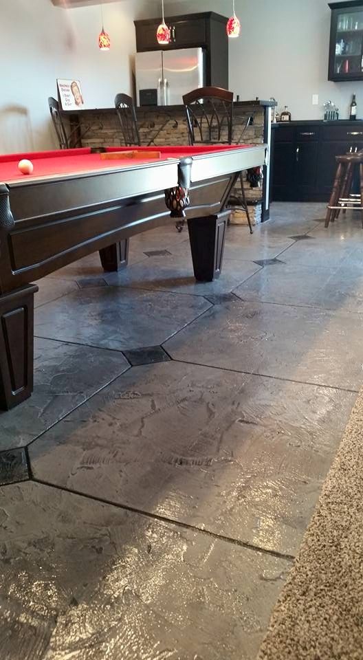 Pool table in a dimly lit bar with stone flooring and chairs in the background