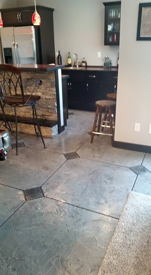 Interior of a kitchen and bar area with stone tile floor, wooden stools, and dark cabinets