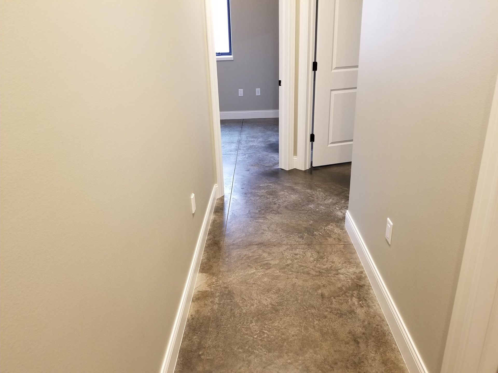 Narrow beige hallway with carpet leading to an open doorway and a room with gray walls.