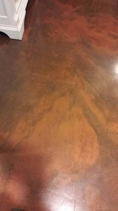 Glossy reddish-brown stained floor with marbled swirls and a white cabinet edge at left