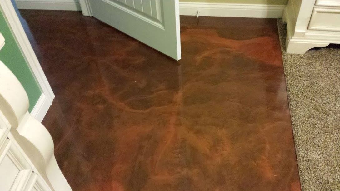 Dark wood-patterned floor in a doorway, with an open white door and beige carpet at the edge.