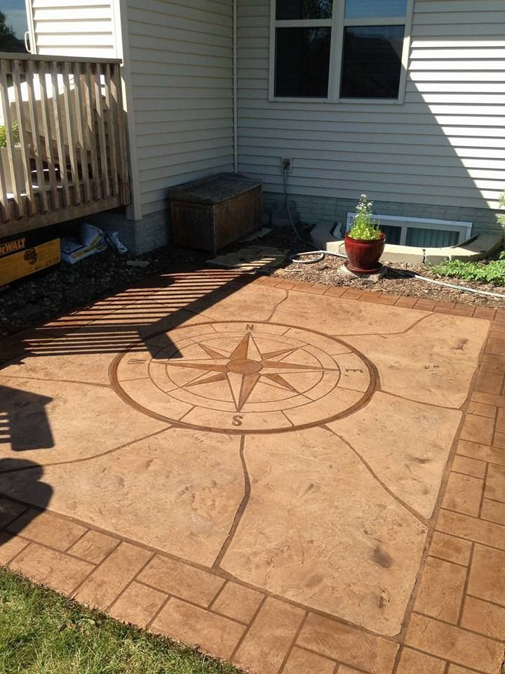 Backyard patio with a compass design stamped in concrete beside a house and wooden deck.