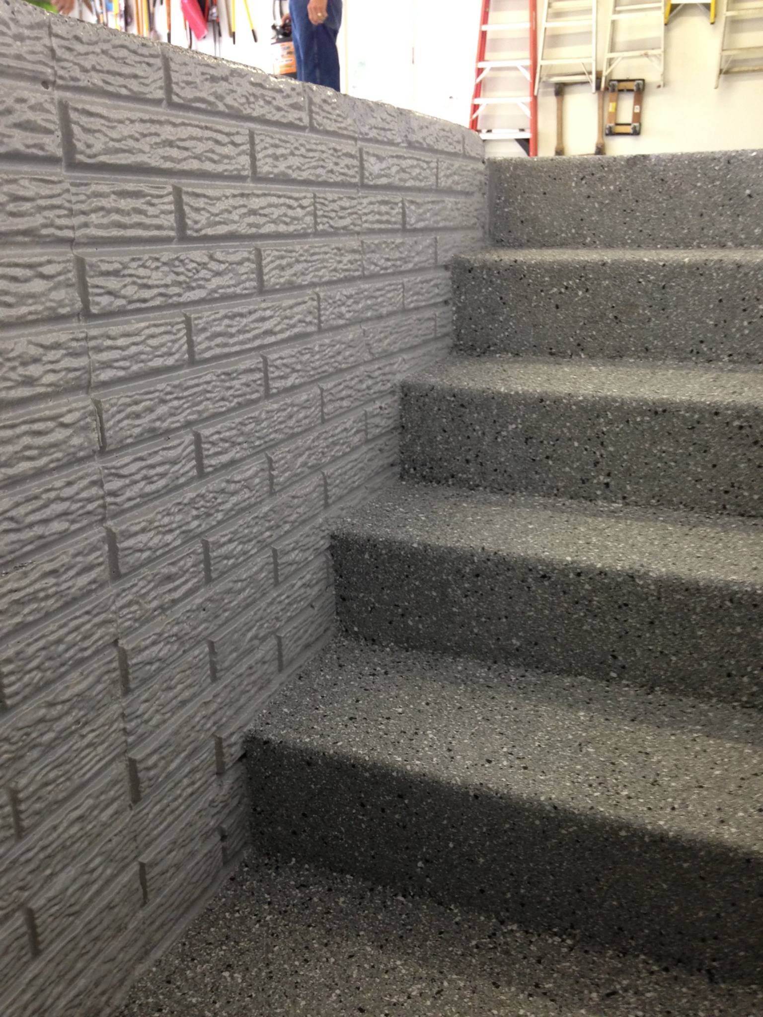 Concrete outdoor stairs beside a gray brick wall, with a beige building in the background.