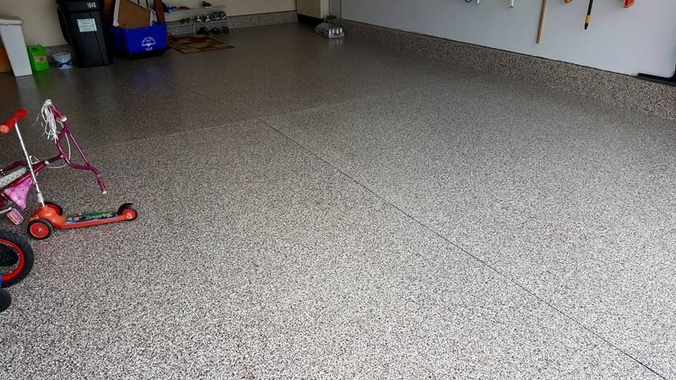 Garage with speckled floor, a red children's scooter on the left, and storage items along the back wall.