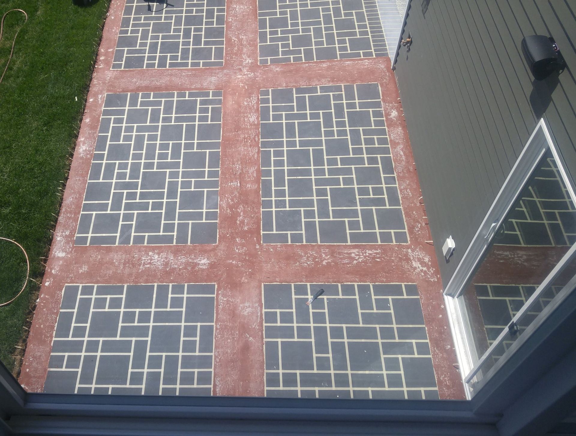Brick and gray paver patio beside a house, viewed from above through a window or door.
