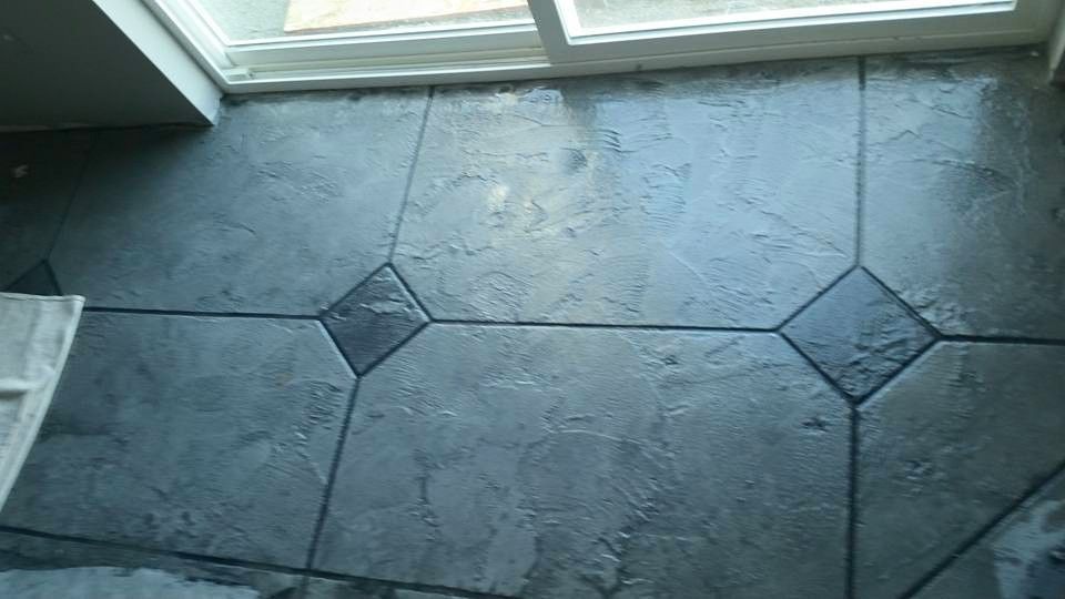 Dark stone tile floor with decorative diamond inlays beside a glass door.