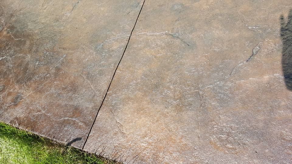 Brown concrete patio with a diagonal crack and a strip of green grass along the edge