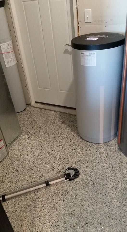 Laundry room with a silver trash can beside a white door and a grabber tool on the floor.
