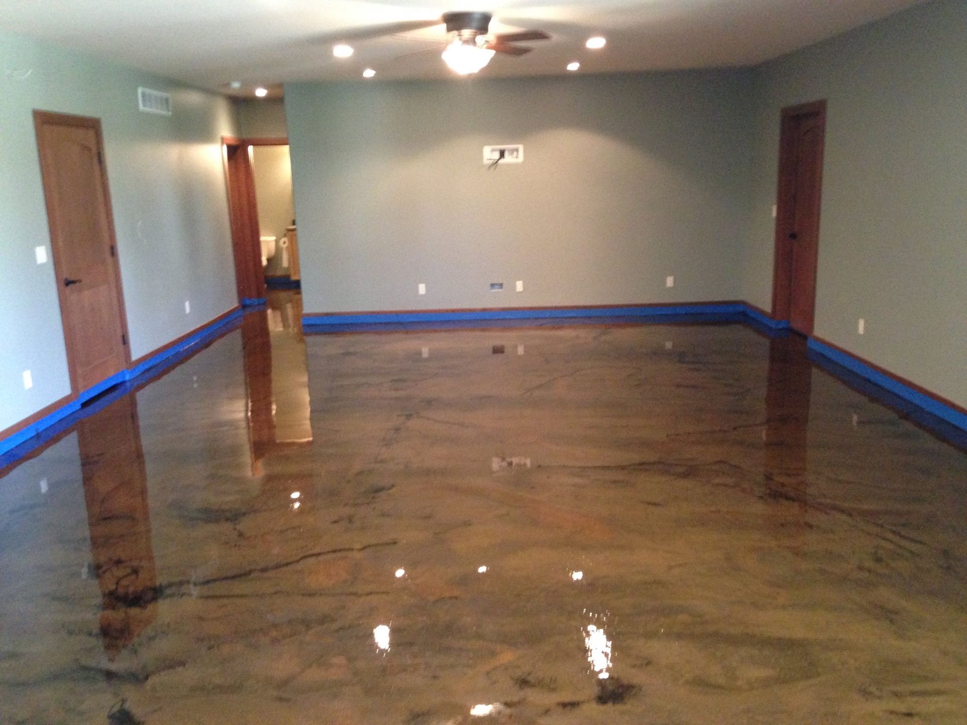 Empty room with a glossy wet floor, gray walls, blue baseboards, and ceiling lights reflected on the surface