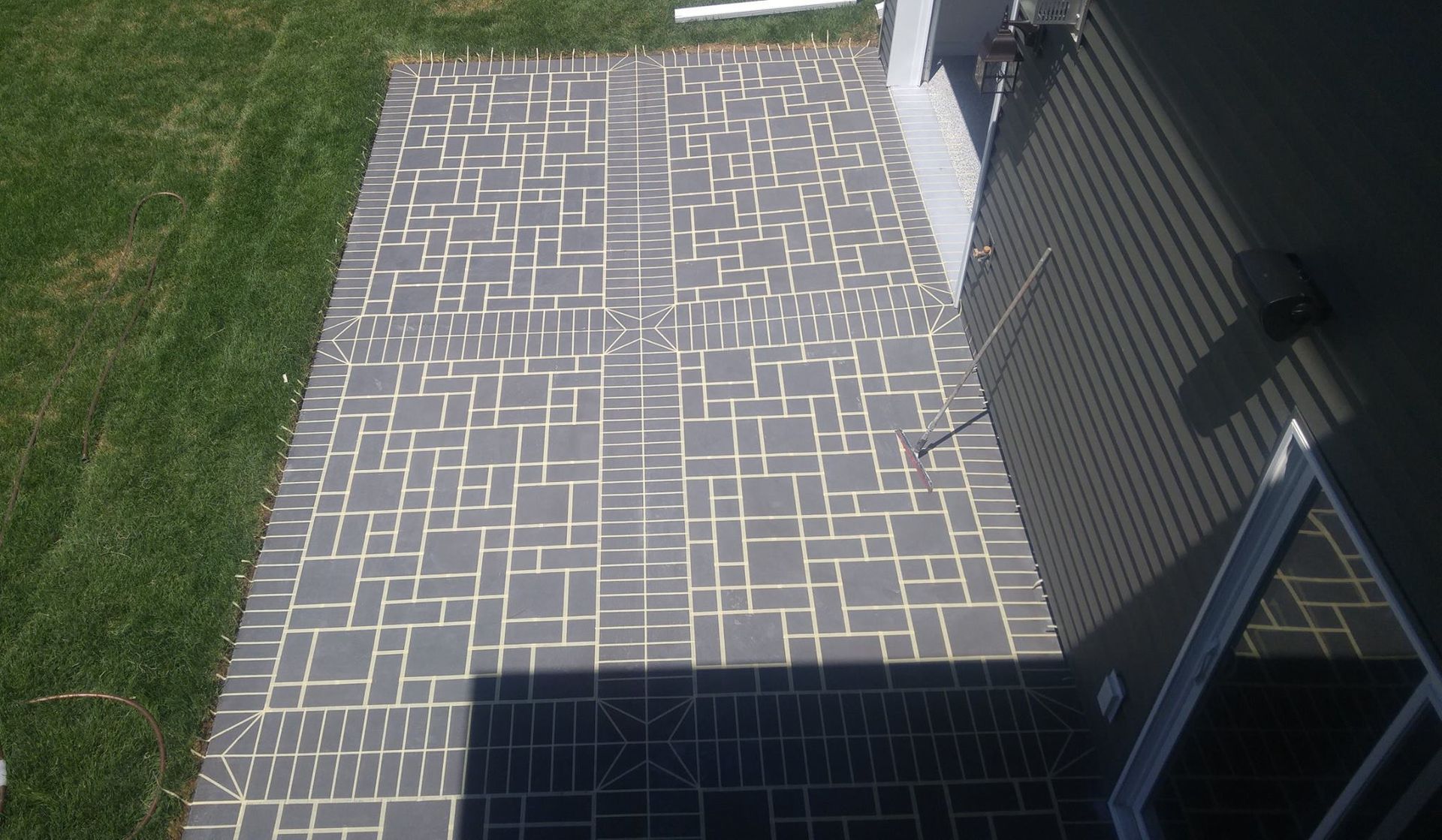 Brick-paver patio beside a grassy lawn, with a dark building wall casting a shadow