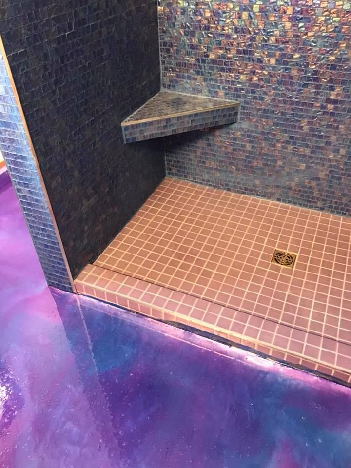Purple-lit shower stall with mosaic tile walls, a tiled bench, and a drain in the floor.