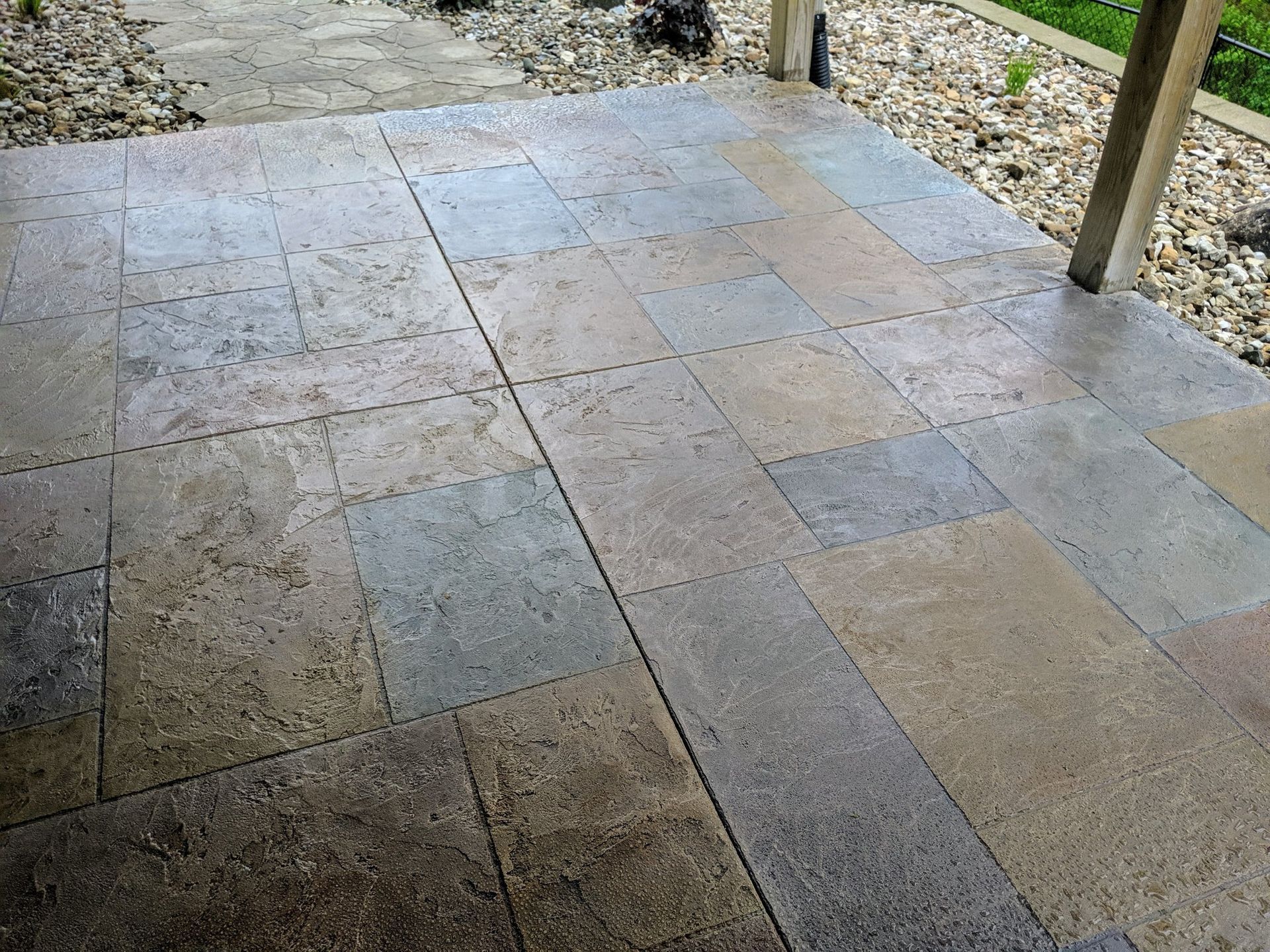 Stone-tiled patio floor with a few wooden posts and gravel edging near a wall