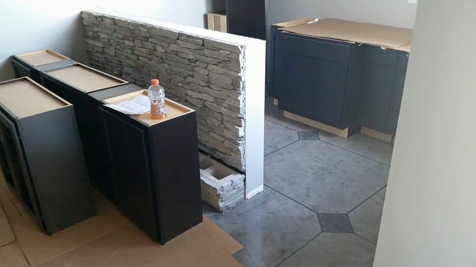 Kitchen cabinets and island panels staged in a room under renovation, with stone accent wall and tiled floor.