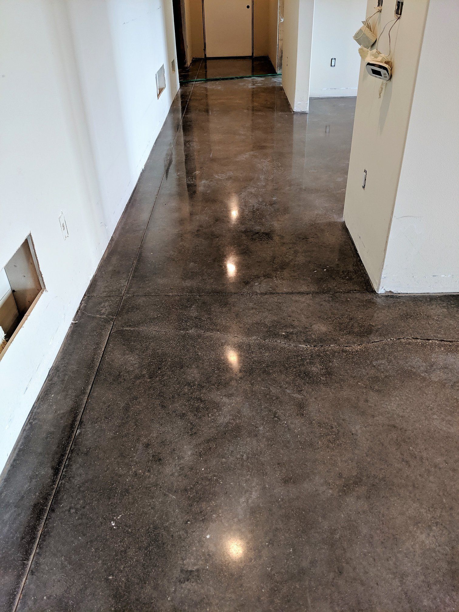 Hallway with polished concrete floor and white walls, showing a doorway and open door on the right.