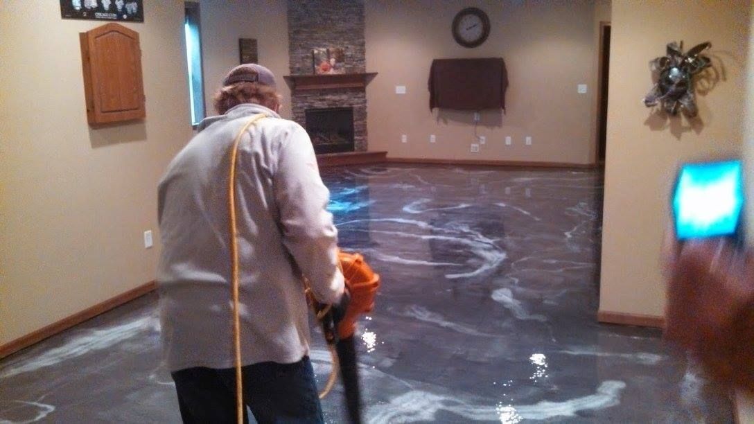 Person using a floor buffer in a mostly empty room with a dark, wet floor