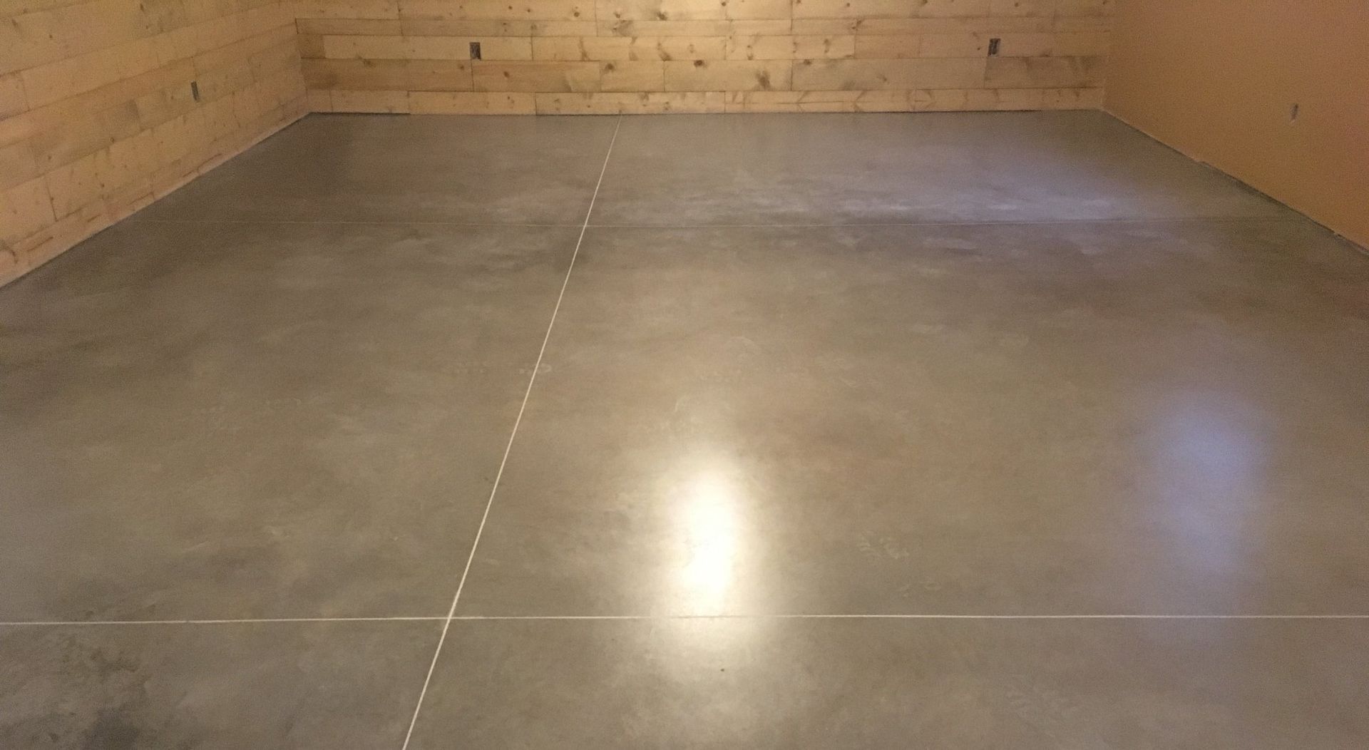 Empty indoor room with gray tiled floor and wooden walls, reflecting light on the surface