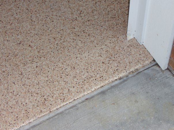 Speckled beige floor meets gray concrete at a doorway threshold