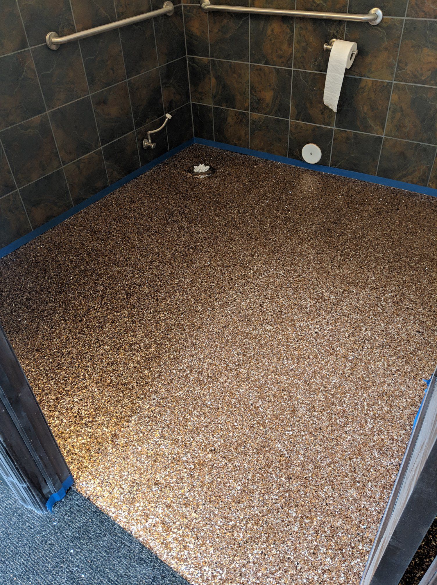 Small tiled shower stall with a pebble floor and a blue door frame.