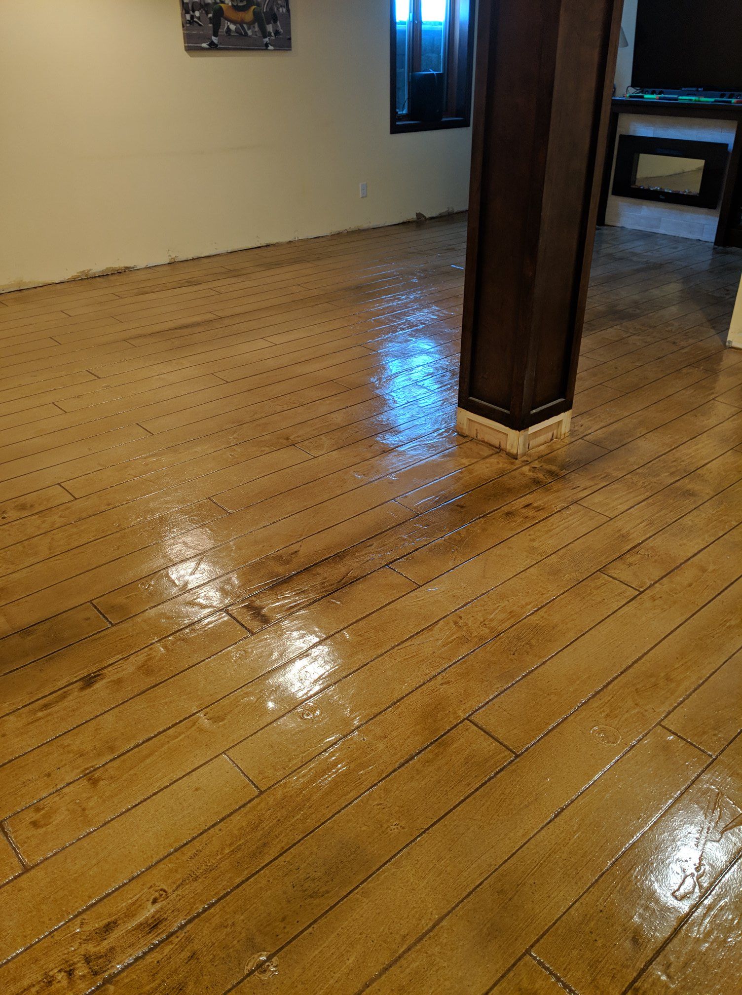 Shiny hardwood floor in an empty room with beige walls and a dark wooden support column.