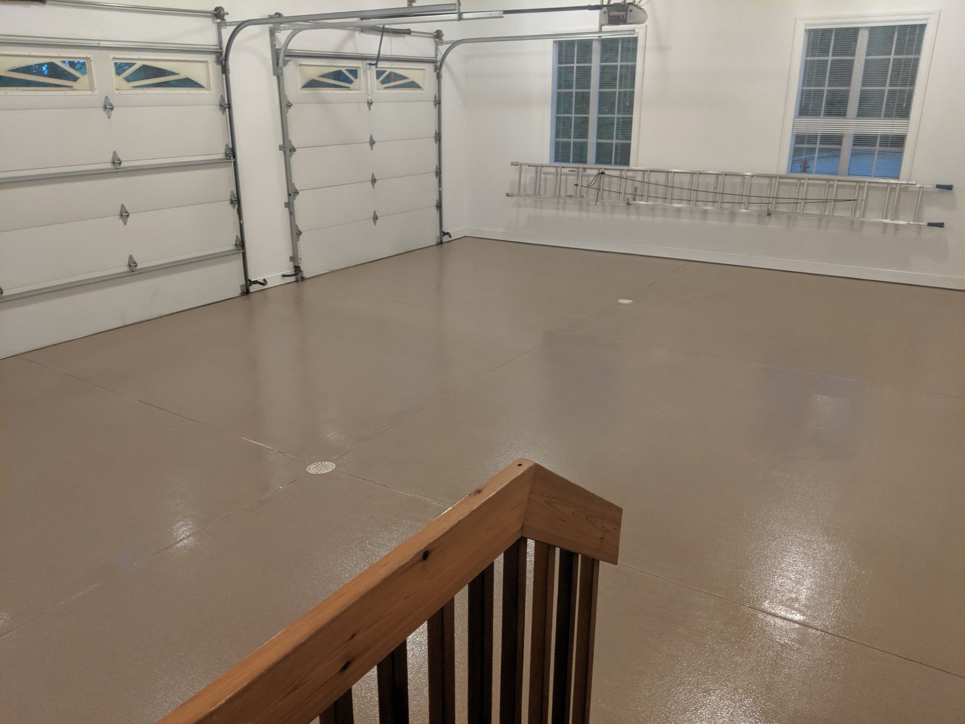 Empty garage with beige floor, white doors, and windows, viewed from a stair landing.