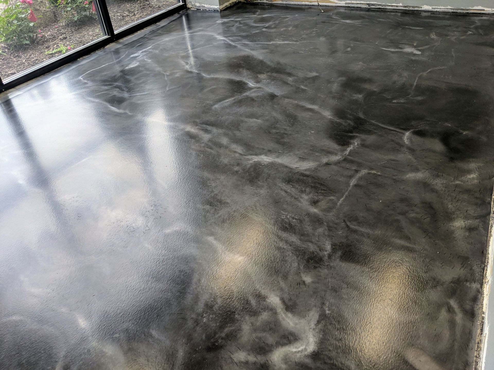 Wet black concrete floor with reflections and a few light patches near a fence.