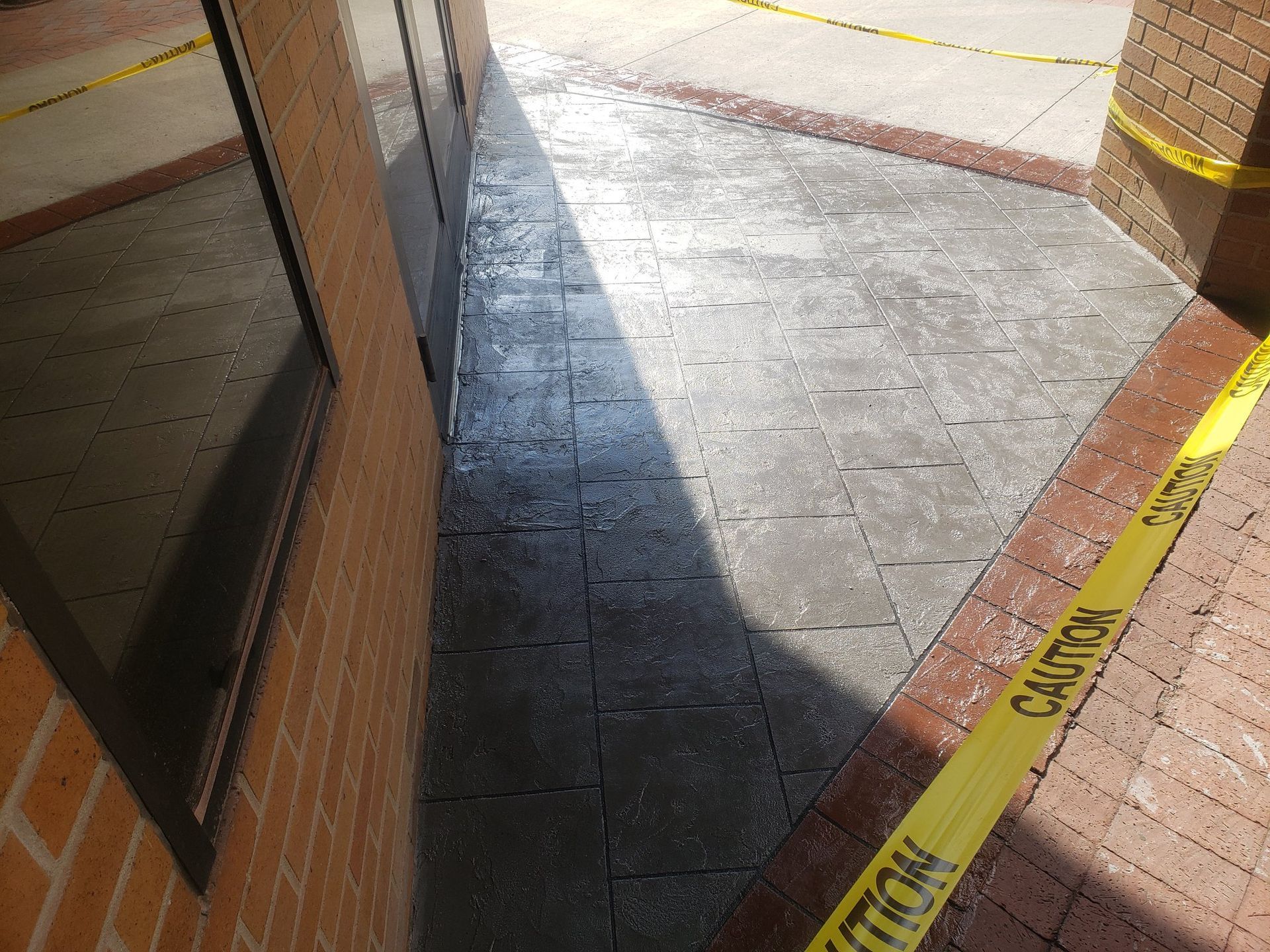 Sunlit concrete walkway beside a building, marked with yellow caution tape and shadows