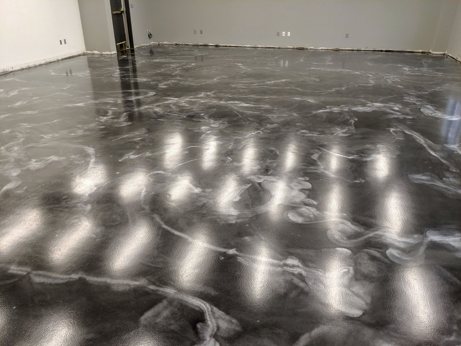 Empty room with a glossy black epoxy floor reflecting overhead lights.