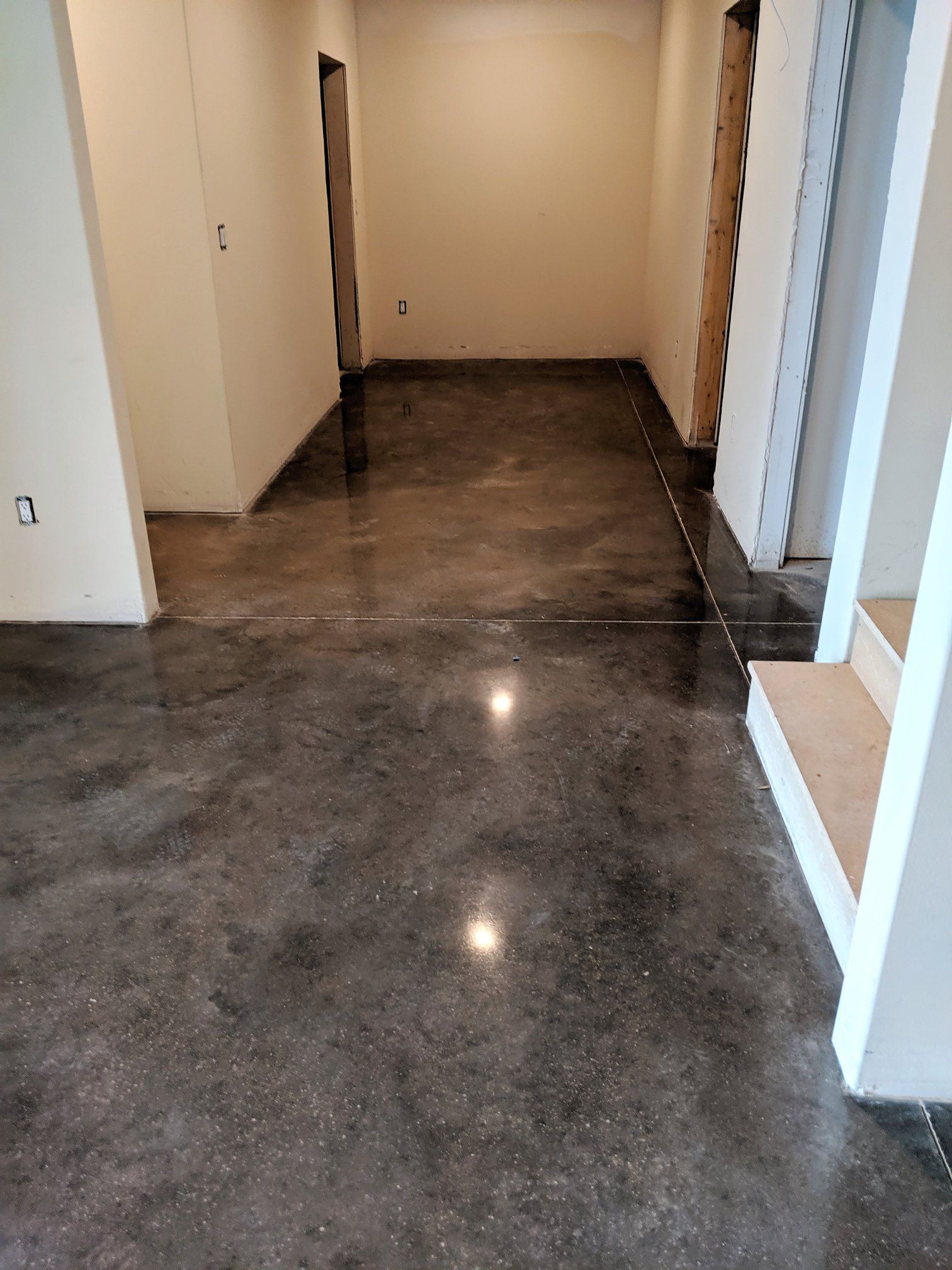 Empty hallway with glossy dark concrete floor and beige walls, viewed toward a closed door.