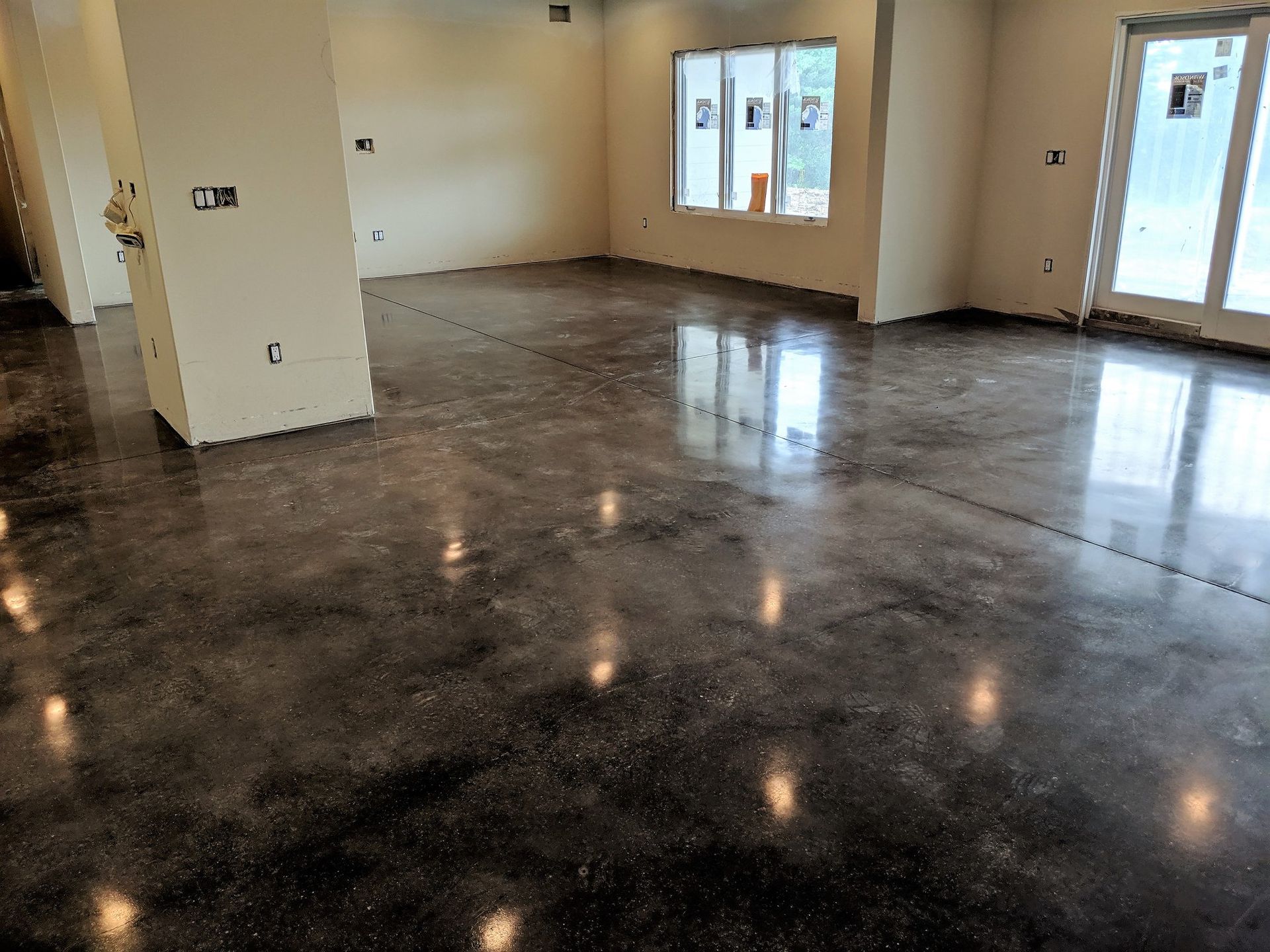 Empty room with glossy dark floor, beige walls, and windows letting in daylight.