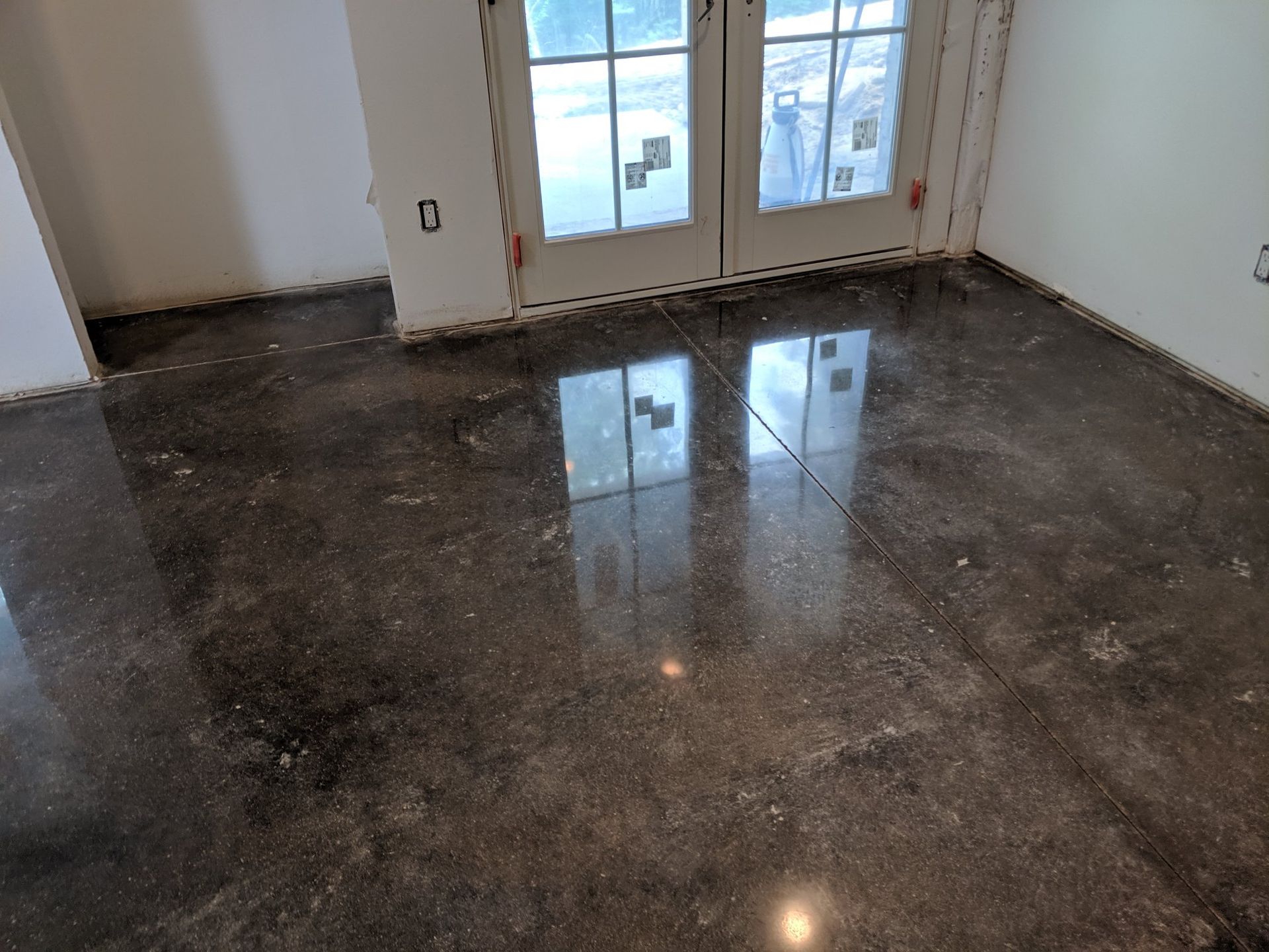 Empty room with glossy dark tile floor and glass doors at the back.