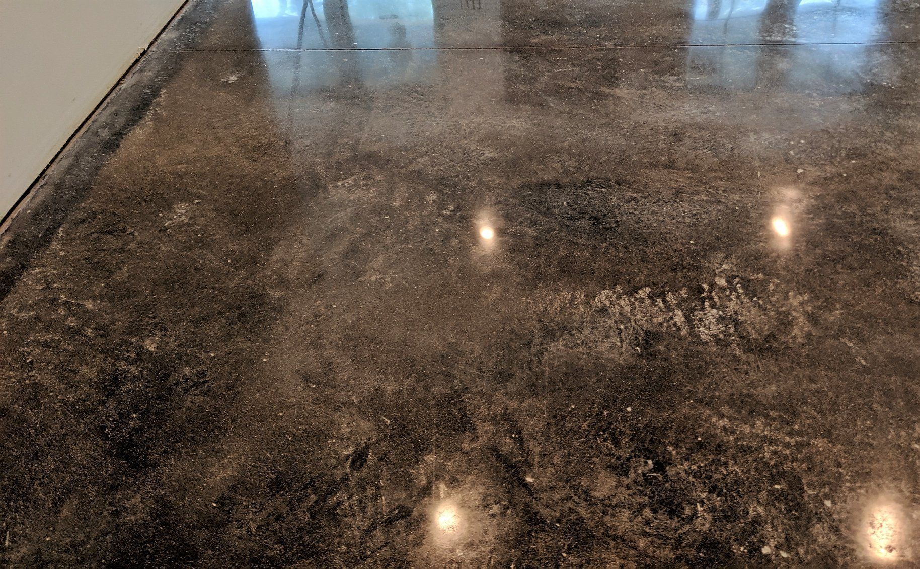 Polished dark granite floor reflecting overhead lights near a wall and doorway