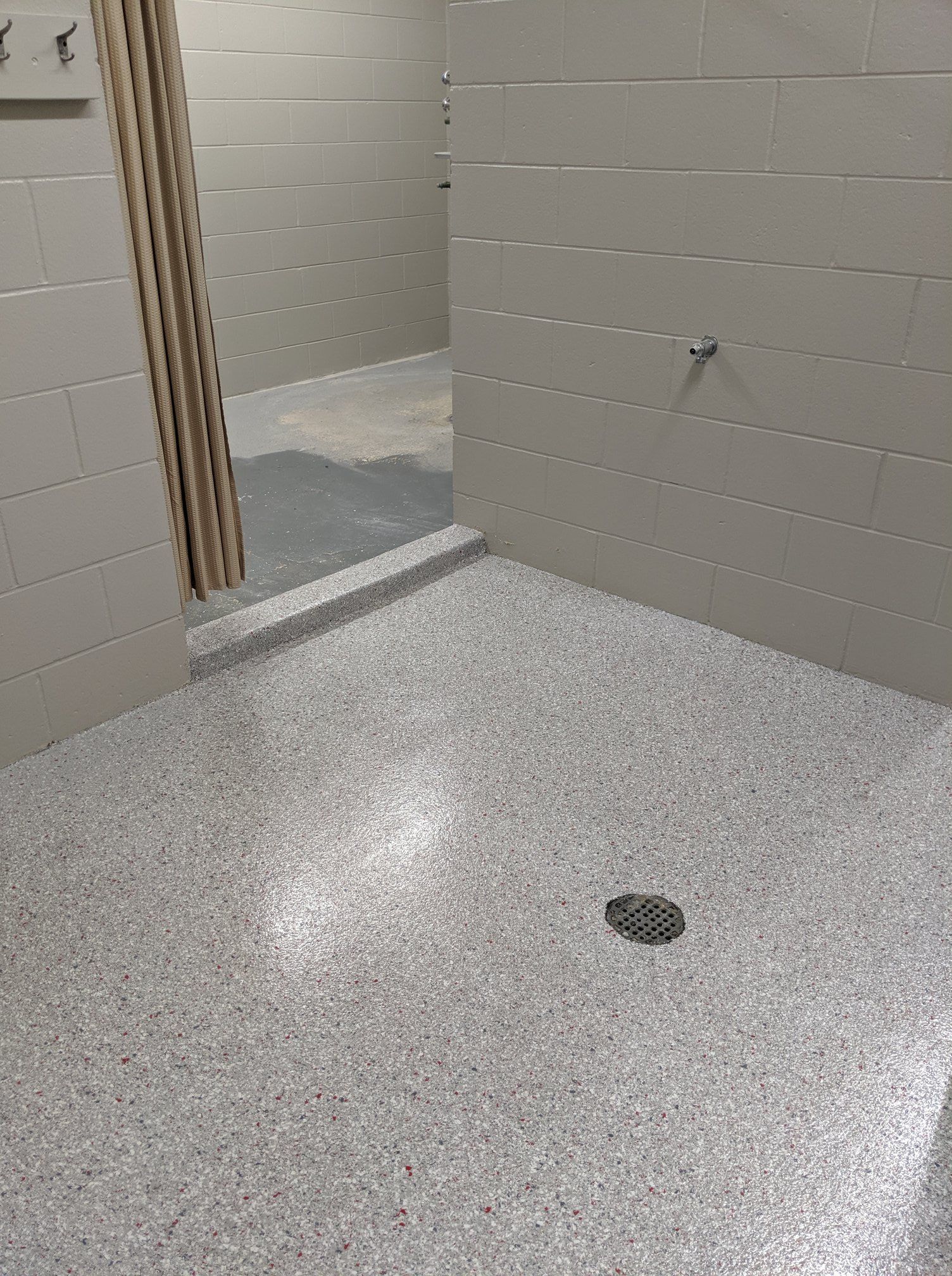 Empty restroom with light gray cinderblock walls and speckled floor, showing an open doorway and floor drain.
