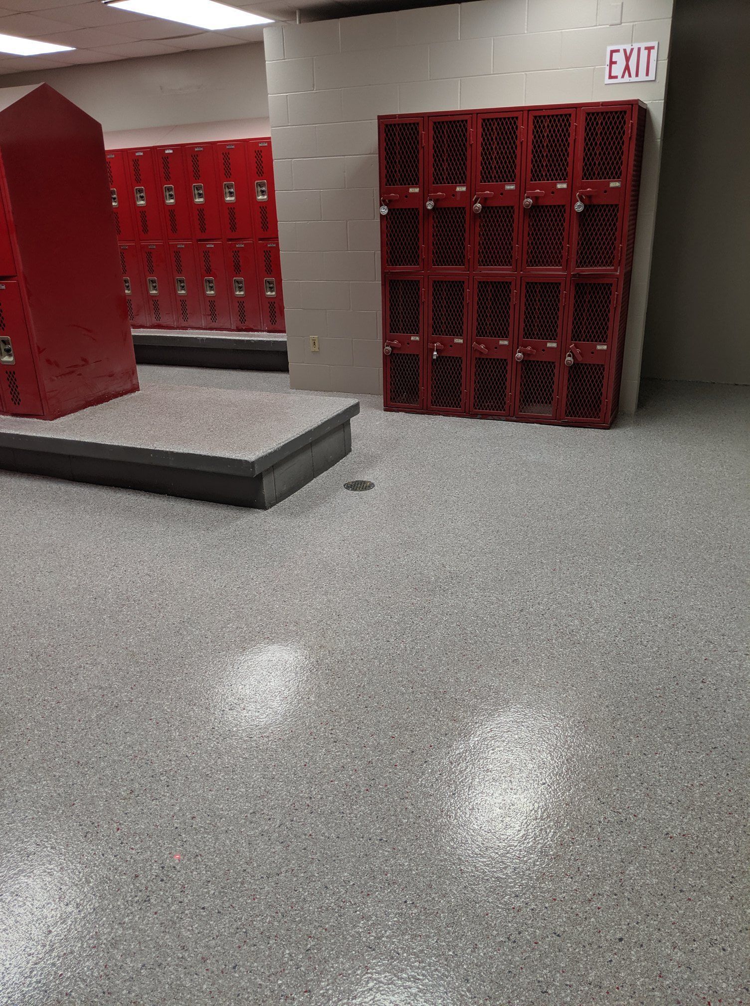 School hallway with red lockers, gray floor, and a small platform under an exit sign.