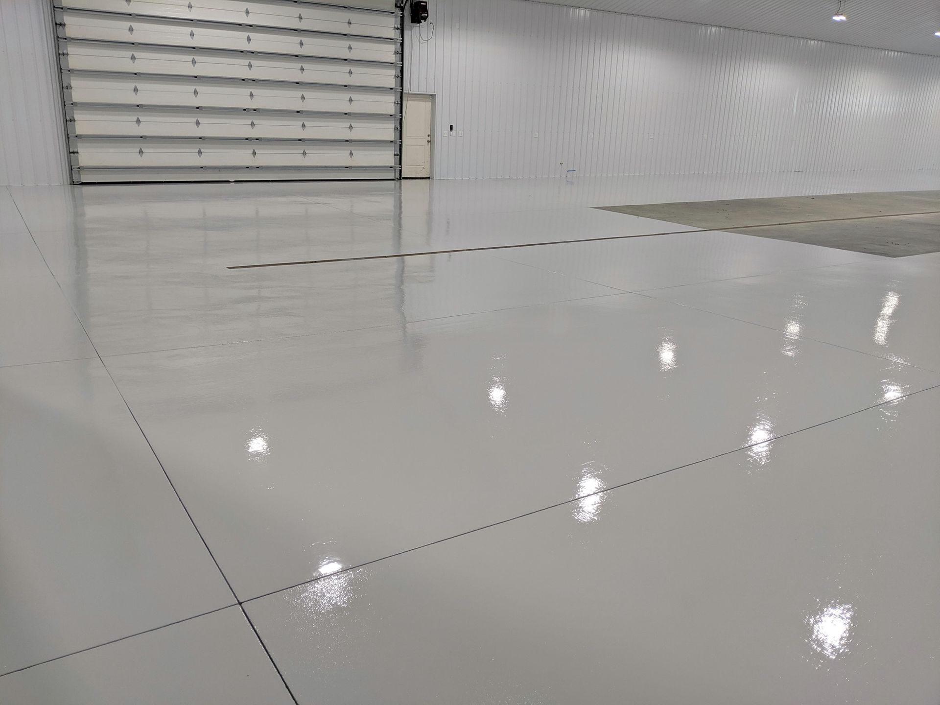 Empty glossy warehouse floor with large white overhead door and bright reflections