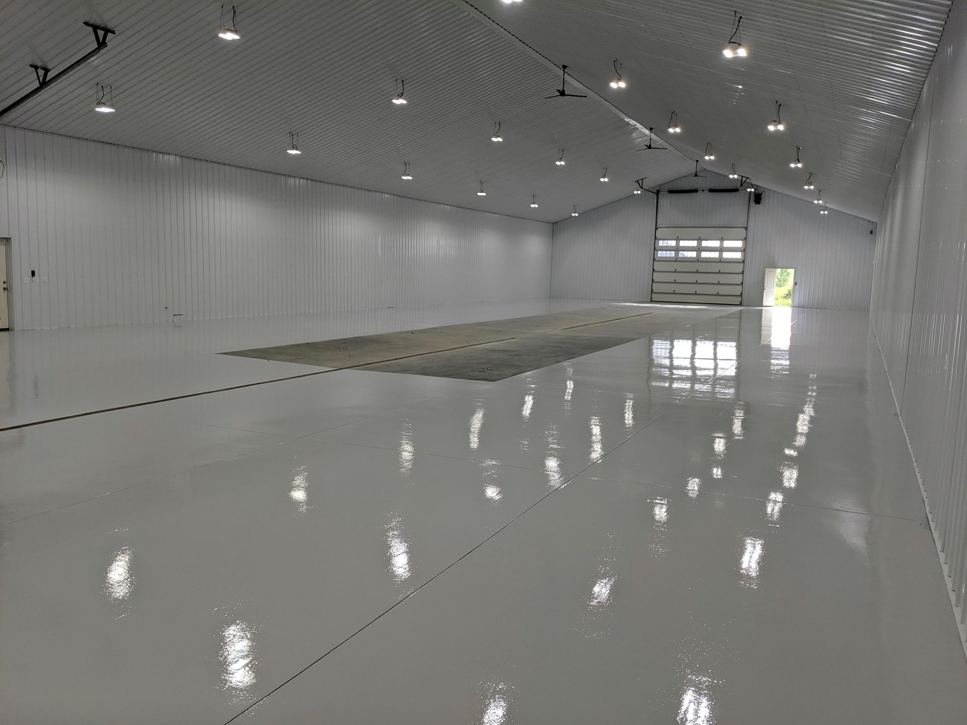 Empty white industrial warehouse with glossy floor and overhead lights