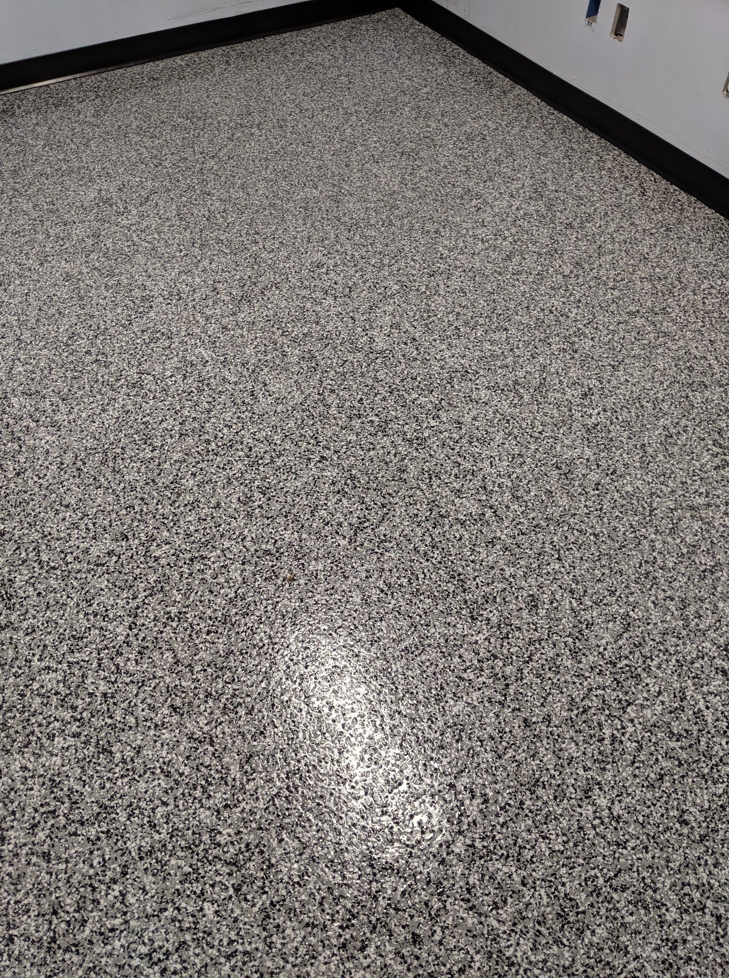 Gray speckled floor with a bright light reflection near the center and a wall edge at the top right