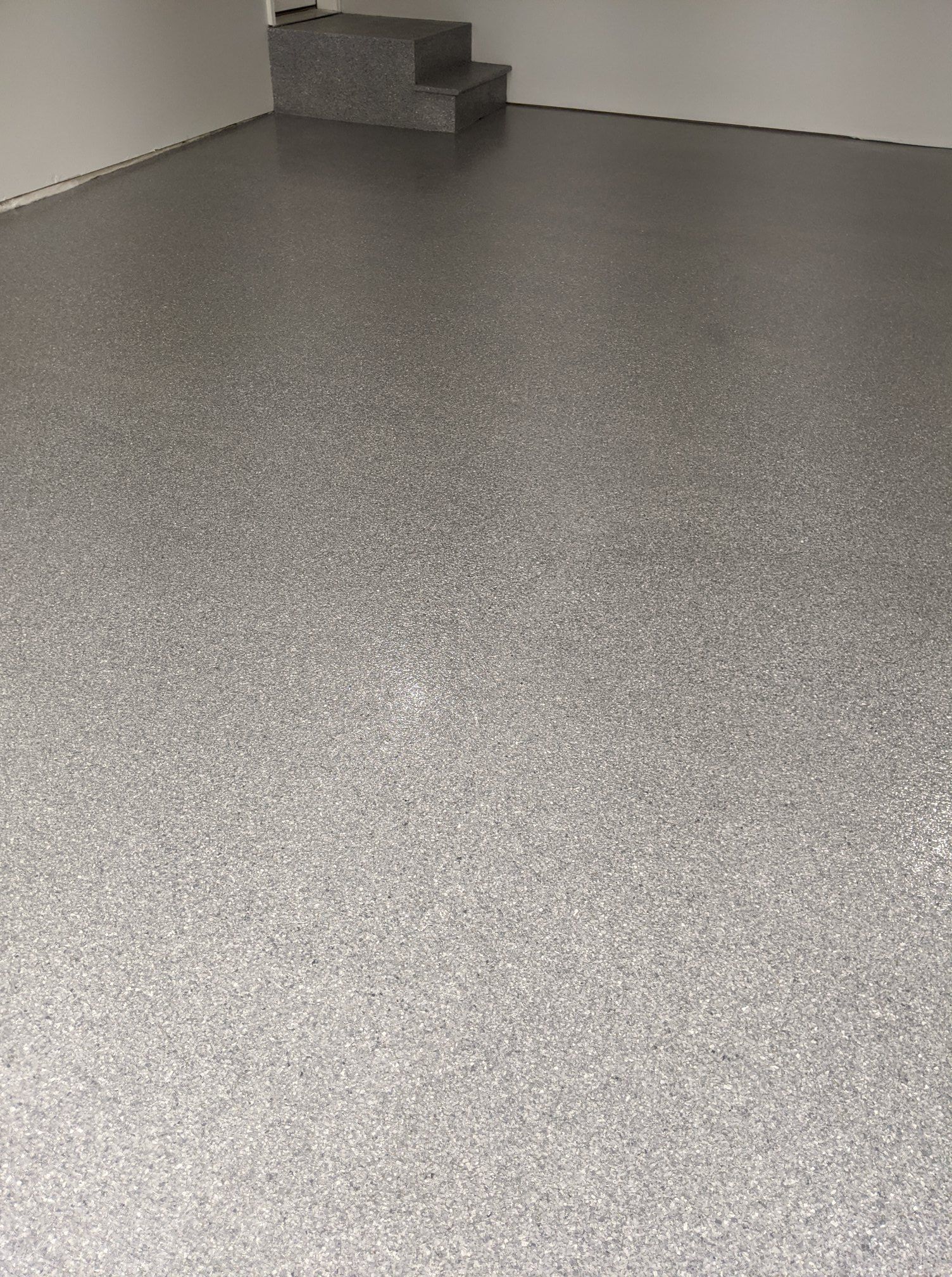 Empty speckled gray floor in a plain indoor room, with a small step or platform in the back corner.