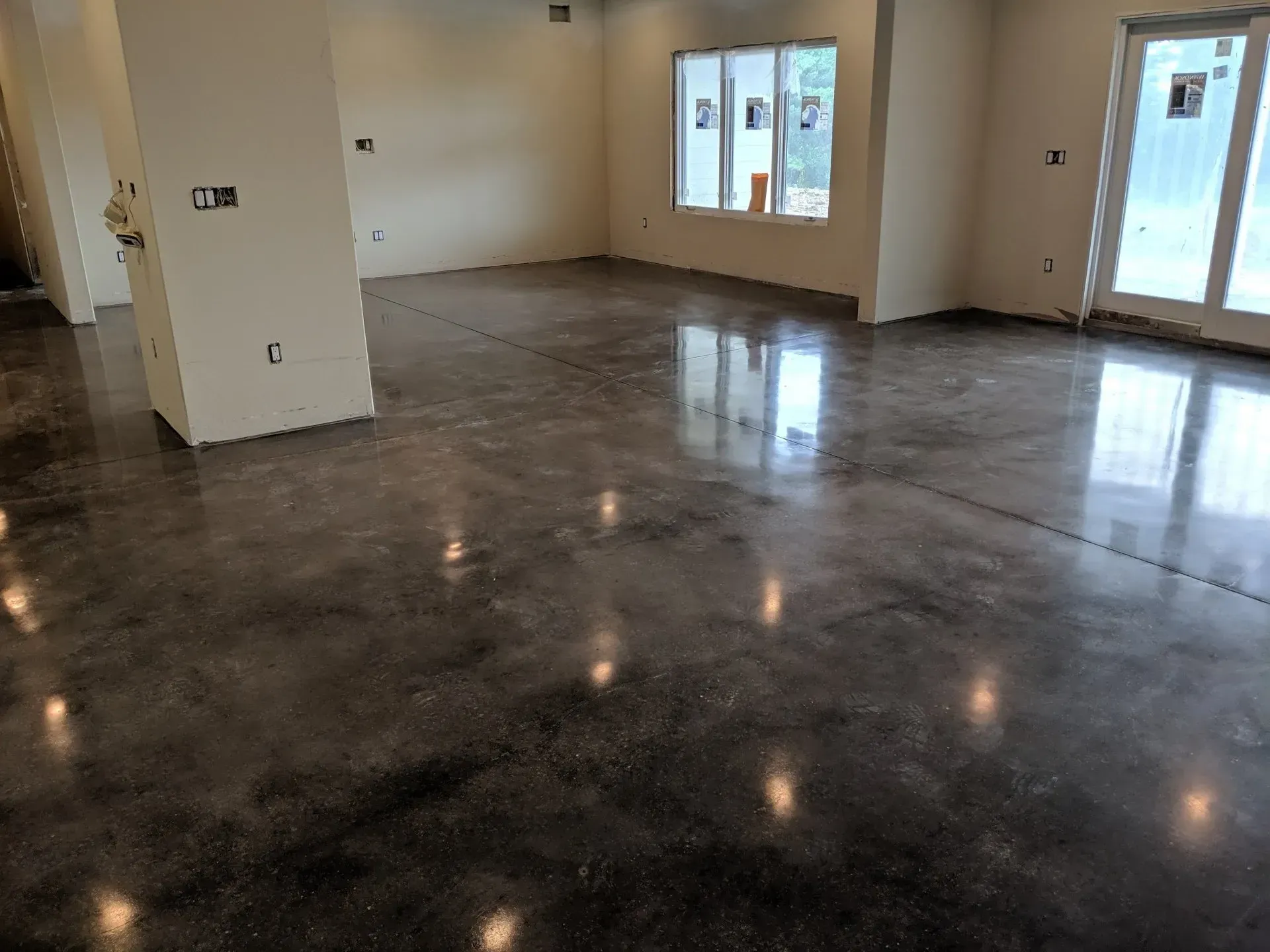 Empty room with glossy dark concrete floor, beige walls, windows, and a door leading outside.