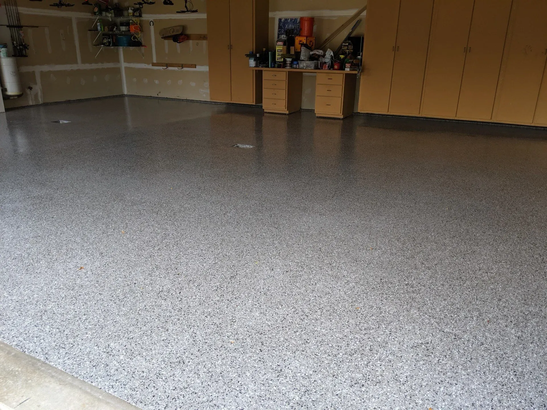 Empty indoor room with a speckled gray floor, wooden cabinets, and shelves along the back wall