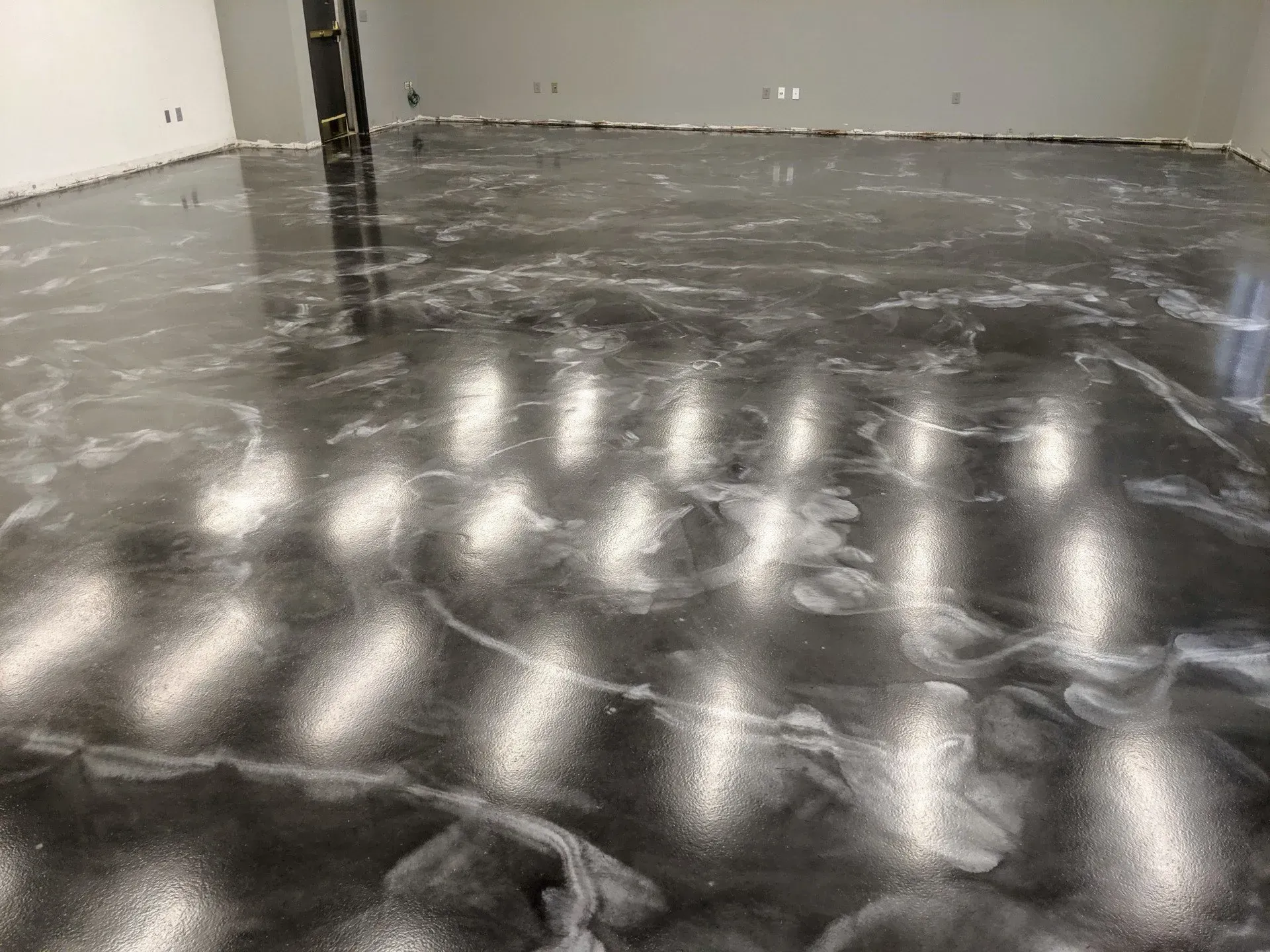Empty room with a glossy black floor reflecting overhead lights and white walls