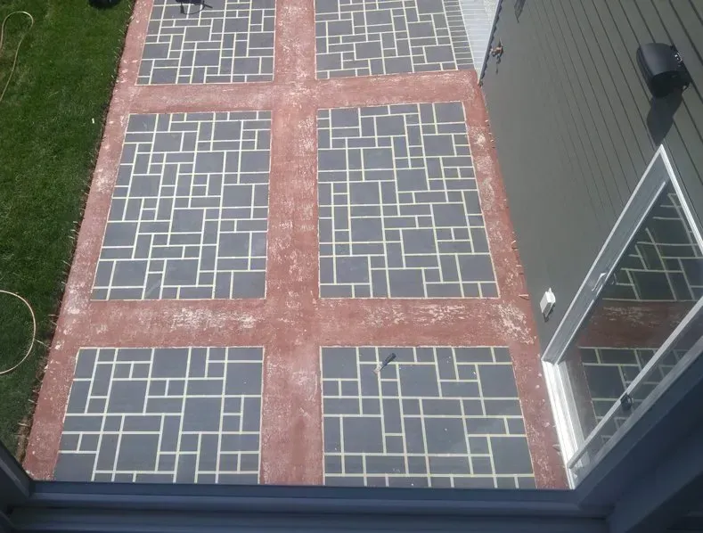 Overhead view of a brick patio with dark pavers and red brick borders beside a house and lawn