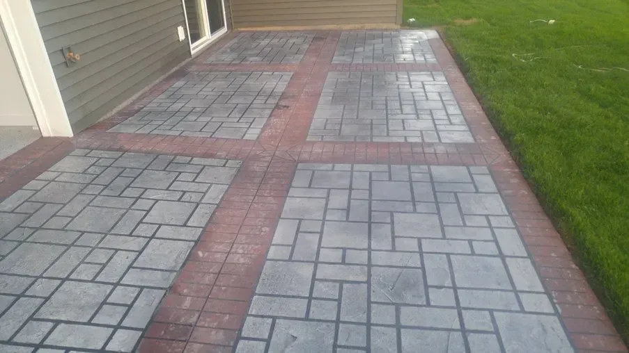 Brick paver walkway beside a house, bordered by grass and a garage door.